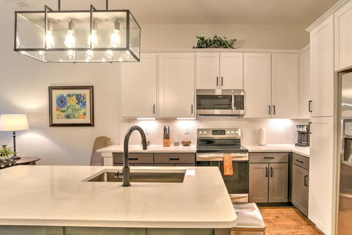 A modern kitchen with a spacious island, contemporary light fixture, stainless steel appliances, and vibrant artwork on the wall. The open layout is inviting for casual meals, coffee breaks, or creative brainstorming sessions.