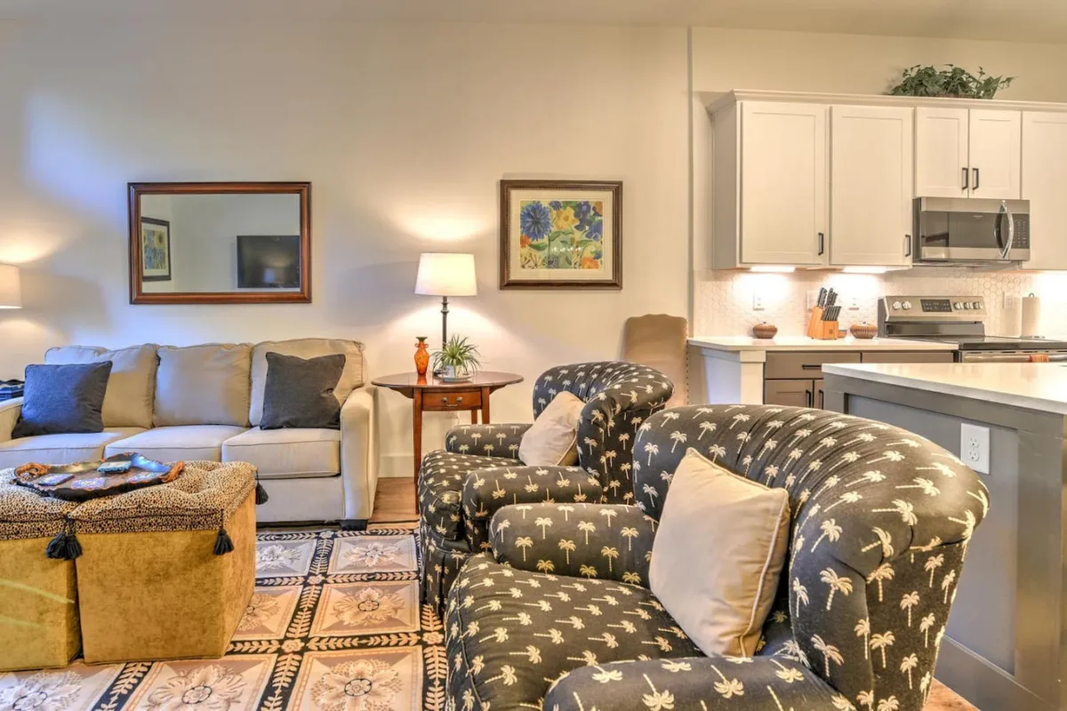 This inviting interior scene features a cohesive open-concept living space with a plush sofa, armchairs, a coffee table, and an adjacent kitchen area. Framed artwork, tasteful decor, and warm lighting create a welcoming ambience ideal for relaxing, socializing, or enjoying meals.