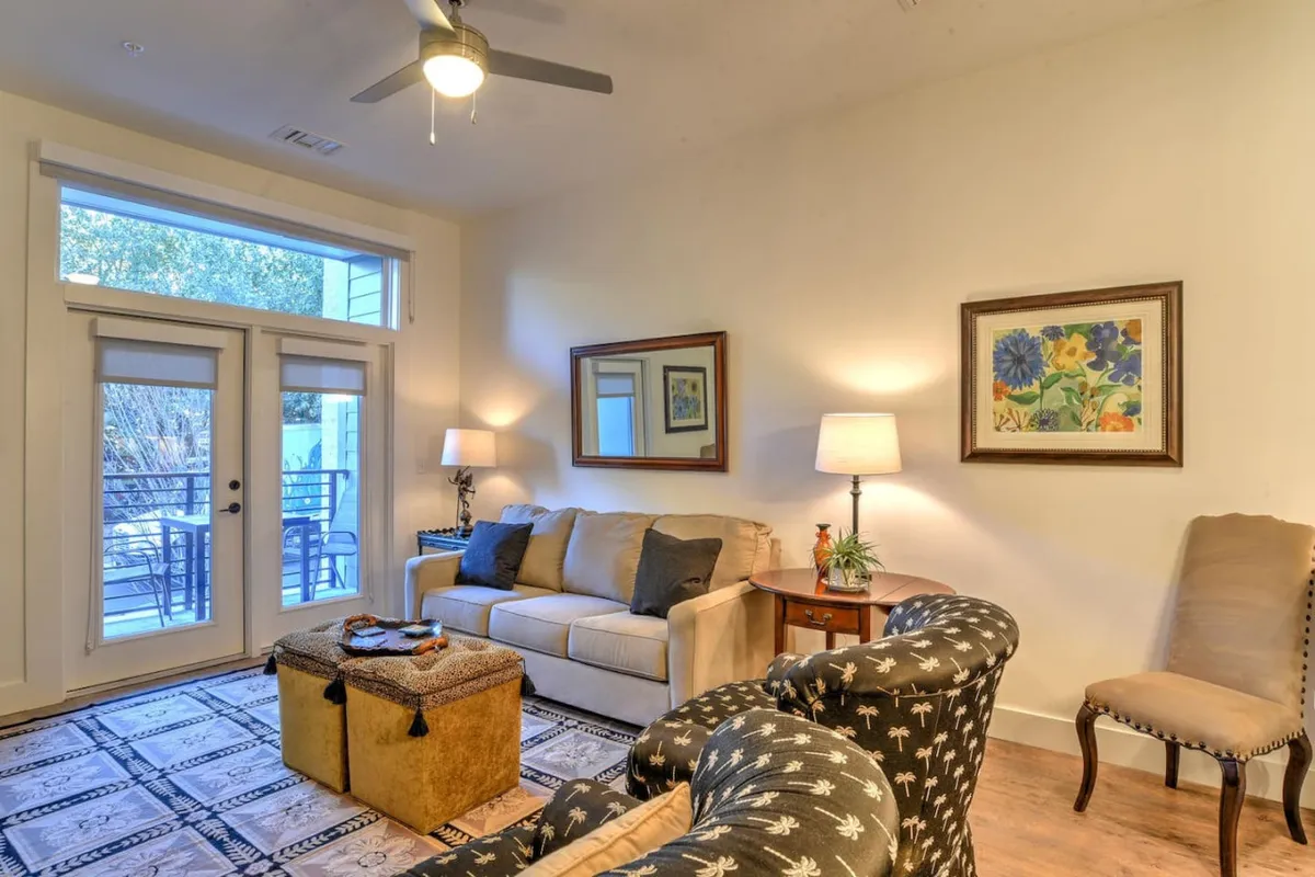 A cozy living area with a sofa, coffee table, armchair, and artwork, featuring sliding doors to the outside. The space is bathed in natural light, with the doors suggesting a seamless connection to an outdoor view or balcony.
