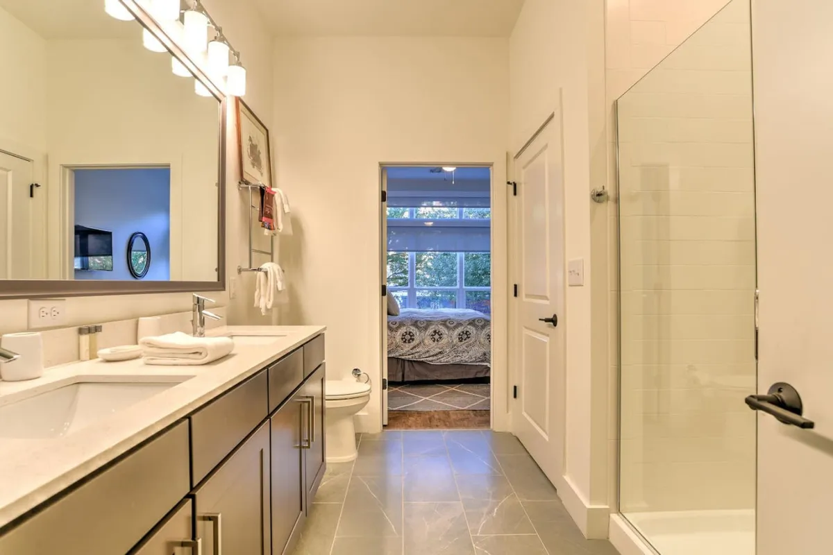 A modern bathroom with an inviting vanity and sink, a sleek shower enclosure, and a doorway that hints at the adjoining bedroom. The design is clean and serene, with soft lighting that creates a spa-like atmosphere, perfect for morning routines or unwinding after a long day.