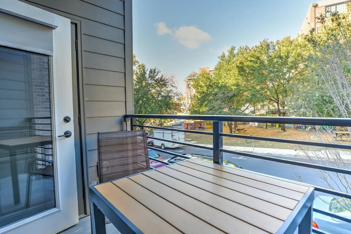 A private balcony featuring comfortable outdoor furniture with an open door leading inside. The view includes leafy treetops and hints of the vibrant urban environment below, capturing the feeling of a secluded yet connected urban perch.