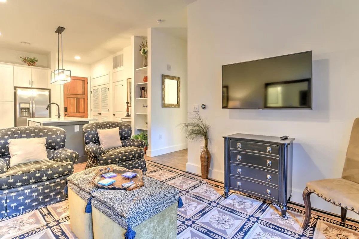 This image features a cozy living area furnished with a plush sofa, a sleek coffee table, a wall-mounted TV, and a decorative mirror that brightens the space. The inviting setting is ideal for relaxing, working remotely, or enjoying a morning coffee while planning the day's urban adventures.