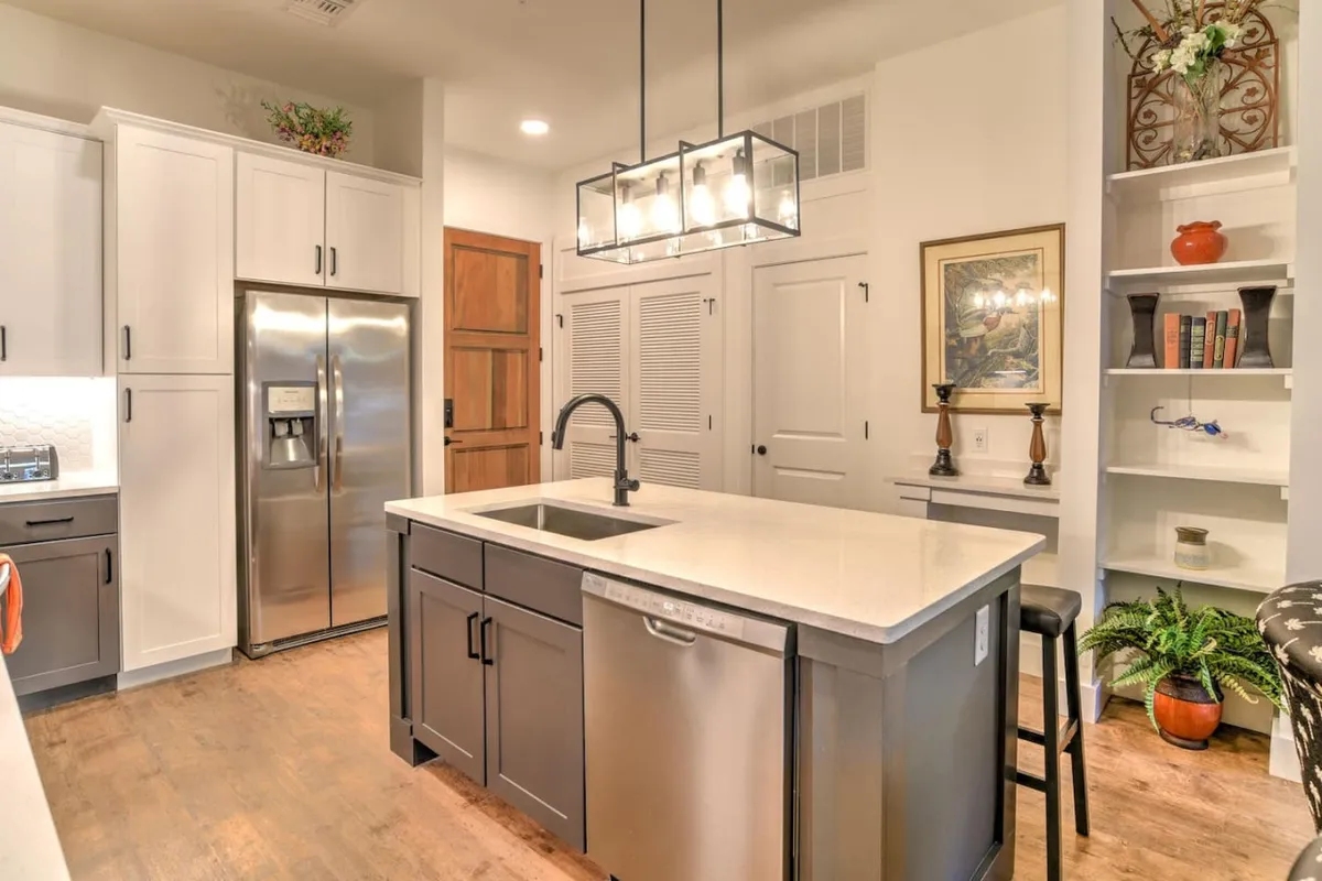 A spacious, modern kitchen with a central island, stainless steel appliances, open shelving, and a striking lighting fixture. The design is bright and functional, offering plenty of room for cooking and gathering.