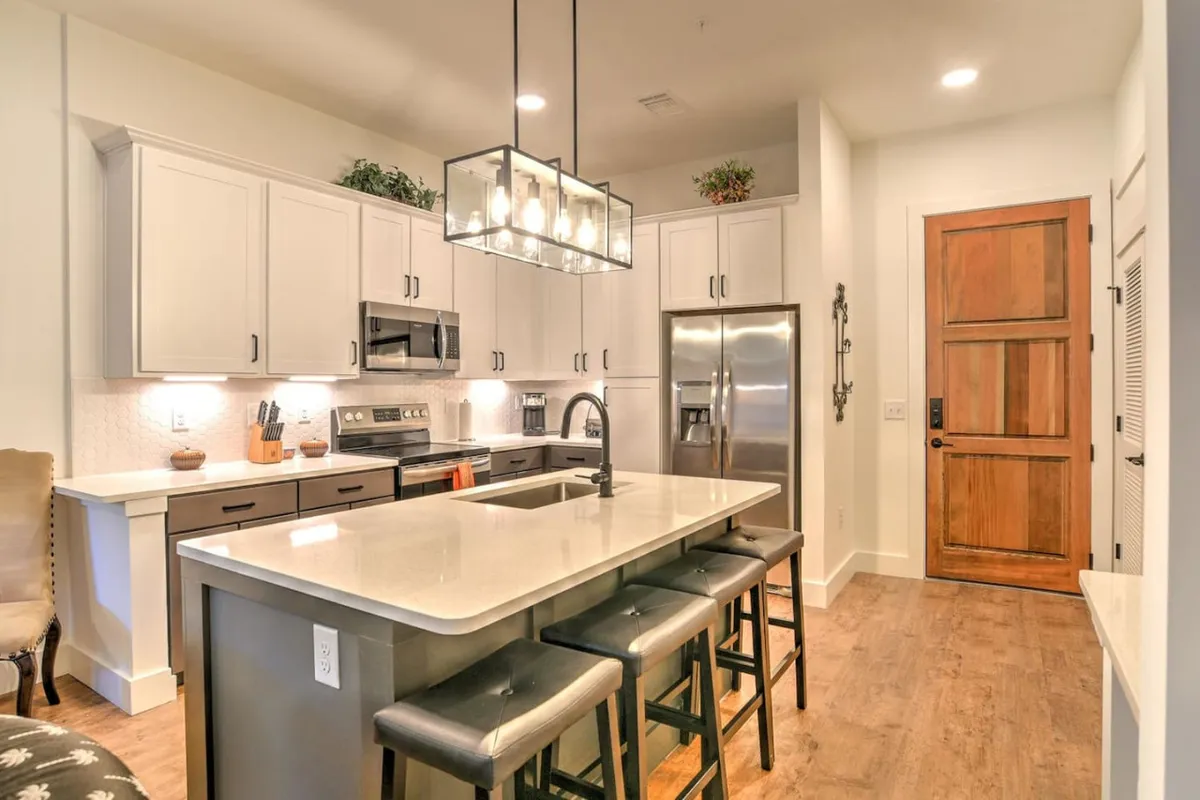 A cozy open kitchen area with a large island countertop, pendant lighting, and sleek stainless steel appliances. The setting is perfect for small gatherings, informal meetings, or unwinding after hours.